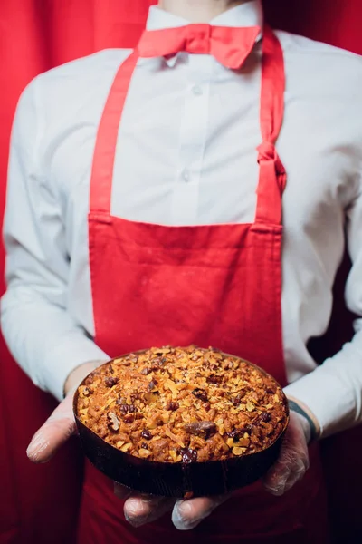 Baker mantém uma bandeja com homem de pão fresco em padeiro uniforme vermelho e branco segurando uma bandeja com panificação — Fotografia de Stock