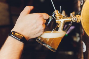 Barmen elini bira fıçısına koyup bira dökerken yakın plan..