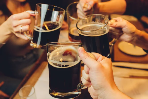 Maschio gruppo clinking bicchieri di birra scura e leggera a tavola . — Foto Stock