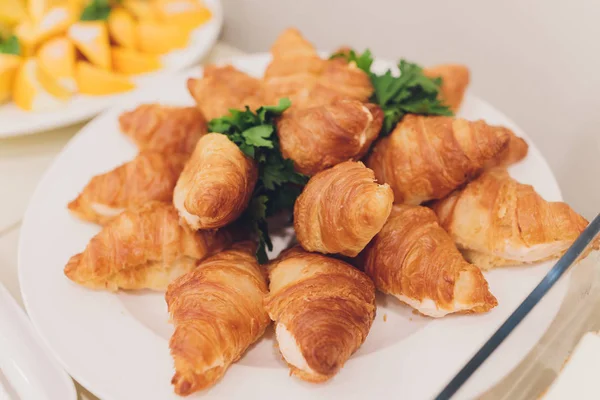 Lots of fresh croissants on a white plate on the buffet in the restaurant. — Stock Photo, Image