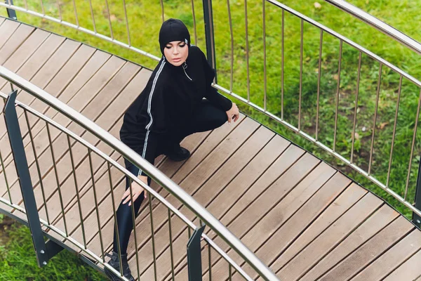 Hidzsáb lány gyakorol a sétányon kora reggel. Muszlim nő visel sport ruhák csinál stretching edzés szabadban. — Stock Fotó