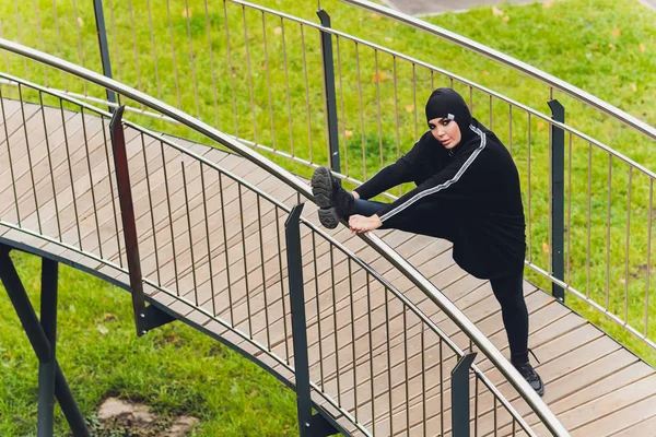 Hidzsáb lány gyakorol a sétányon kora reggel. Muszlim nő visel sport ruhák csinál stretching edzés szabadban. — Stock Fotó