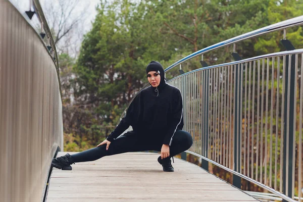 Hijab menina exercitando-se na ponte passarela no início da manhã. Mulher muçulmana vestindo roupas esportivas fazendo exercícios de alongamento ao ar livre . — Fotografia de Stock