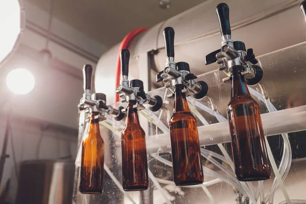 Εργοστάσιο ζυθοποιίας χύνει μπύρα σε γυάλινα μπουκάλια σε γραμμές μεταφοράς. Βιομηχανική εργασία, αυτοματοποιημένη παραγωγή τροφίμων και ποτών. Τεχνολογικές εργασίες στο εργοστάσιο. — Φωτογραφία Αρχείου
