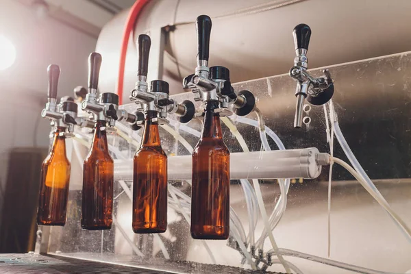 Brouwerij fabriek morst bier in glazen flessen op transportbanden. Industrieel werk, geautomatiseerde productie van voedsel en dranken. Technologisch werk in de fabriek. — Stockfoto