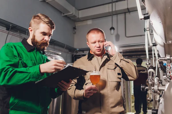 Érett férfi, a kézműves sör a sörgyár minőségének vizsgálata. Felügyelő ellenőrzése sör alkohol gyártási gyárban dolgozik. Man szeszfőzde minőségének ellenőrzéséhez, csapolt sör. — Stock Fotó