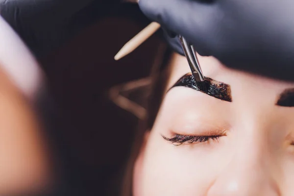 Esthéticienne maquilleuse applique de la peinture au henné sur des sourcils préalablement arrachés, design, taillés dans un salon de beauté lors de la correction de session. Soins professionnels pour le visage. — Photo