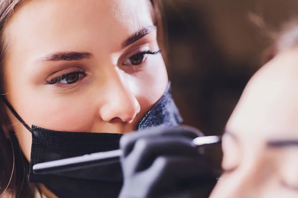 Esthéticienne maquilleuse applique de la peinture au henné sur des sourcils préalablement arrachés, design, taillés dans un salon de beauté lors de la correction de session. Soins professionnels pour le visage. — Photo