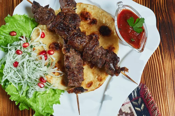 Kebabs de porc maigre en cubes servis avec une tortilla de maïs et une salade de laitue fraîche et de tomates, vue rapprochée sur un fond sombre . — Photo