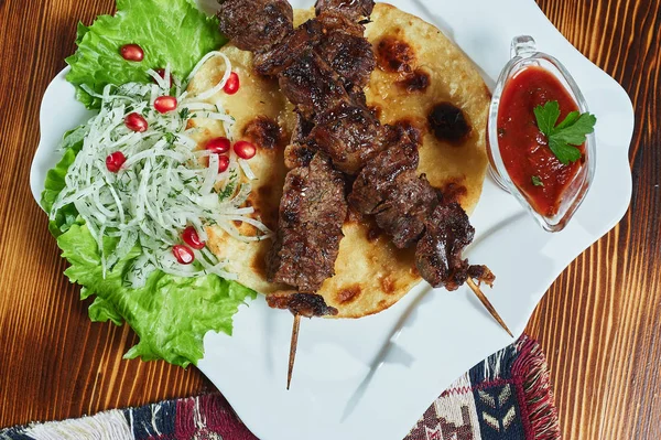 Healthy barbecued lean cubed pork kebabs served with a corn tortilla and fresh lettuce and tomato salad, close up view on a dark background.