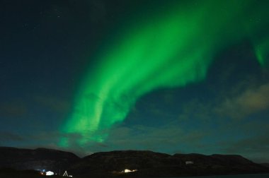 Okyanusun üzerinde Aurora Borealis. Teriberka, Rusya 'nın kuzey ışıkları. Kutup ışıkları ve bulutlarıyla yıldızlı gökyüzü. Aurora 'lı kış manzarası, bulanık sularda taşlı deniz, karlı dağlar. Seyahat