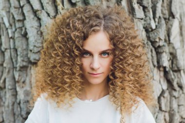 Arkasında ağaçlar olan bir parkta duran genç bir kadının yakın çekimi..