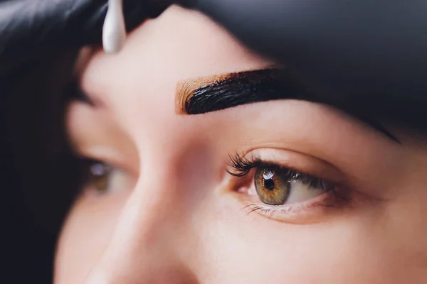 Kosmetikerin - Visagistin trägt in einem Schönheitssalon in der Sitzungskorrektur Farbhenna auf zuvor gepflückte, gestutzte Augenbrauen auf. Professionelle Gesichtspflege. — Stockfoto