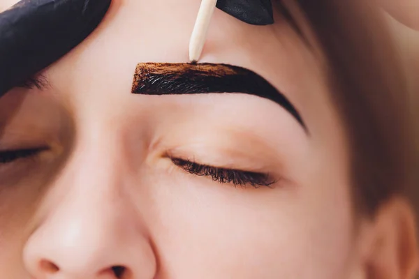 Beautician- maquiador aplica henna pintura em previamente arrancado, design, sobrancelhas aparadas em um salão de beleza na correção sessão. Cuidados profissionais para o rosto. — Fotografia de Stock