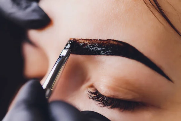 Esteticista-artista de maquillaje aplica henna pintura en previamente arrancado, diseño, cejas recortadas en un salón de belleza en la corrección de la sesión. Cuidado profesional de la cara. —  Fotos de Stock