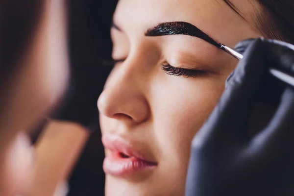 Esthéticienne maquilleuse applique de la peinture au henné sur des sourcils préalablement arrachés, design, taillés dans un salon de beauté lors de la correction de session. Soins professionnels pour le visage. — Photo