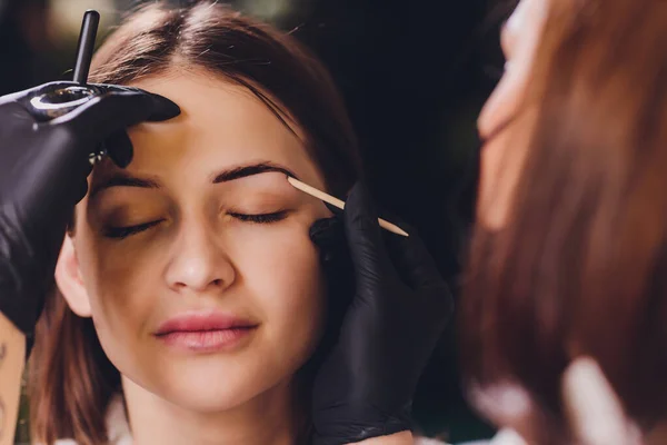 Kosmetikerin - Visagistin trägt in einem Schönheitssalon in der Sitzungskorrektur Farbhenna auf zuvor gepflückte, gestutzte Augenbrauen auf. Professionelle Gesichtspflege. — Stockfoto