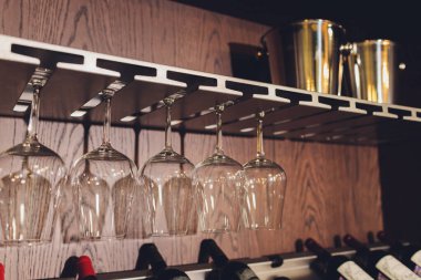 Closeup çok baş aşağı boş şeffaf şeffaf kristal ters şarap bardakları kahverengi ahşap raf, raf, vitrin, paslanmaz çelik korkuluk barda düz sıralar asılı, dolap.