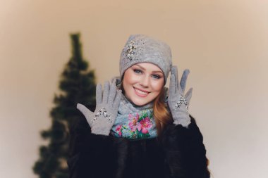 Yana doğru heyecan arayan sürpriz mutlu güzel kadın. Örme sıcak şapka ve gri arka plan üzerinde izole eldivenler giymiş Noel kız.