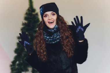 Yana doğru heyecan arayan sürpriz mutlu güzel kadın. Örme sıcak şapka ve gri arka plan üzerinde izole eldivenler giymiş Noel kız.