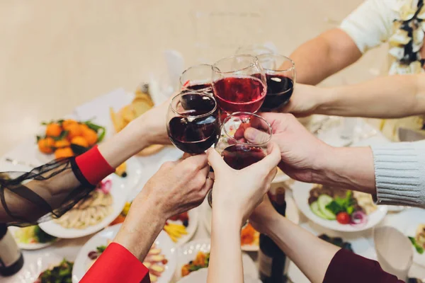 Close-up shot van groep mensen klinkende glazen met wijn of champagne in de voorkant van bokeh achtergrond. handen van ouderen. — Stockfoto