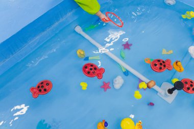 Kürek havuzunda balık tutmak. Havuzda çocuk oyuncakları var. Oyuncak balık oltası. Neşeli çocuklar balık tutuyor, havuzda balık tutuyor..