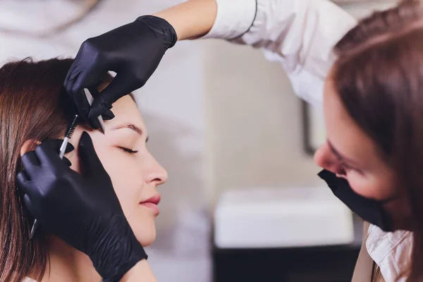 美容师美容师在美容院修整过程中，在先前拔出的、设计、修剪过的眉毛上涂上彩绘指甲油。面部的专业护理. — 图库照片