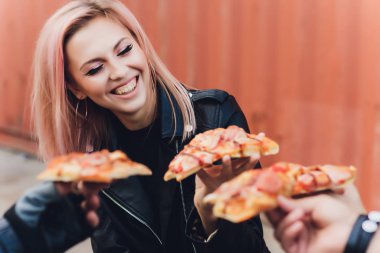 Motosiklette otururken lezzetli bir pizza yiyen kız..