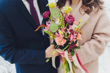 Olağandışı bir gelinin elinde turuncu ve beyaz çiçekli şık buket düğün.