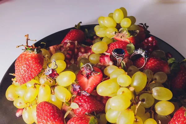 Bovenaanzicht van de twee witgouden trouwringen en één verlovingsring met diamanten geplaatst op de twee rode aardbeien. — Stockfoto