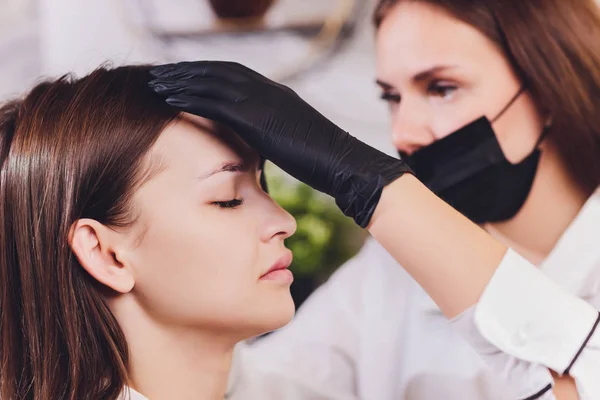 美容师美容师在美容院修整过程中，在先前拔出的、设计、修剪过的眉毛上涂上彩绘指甲油。面部的专业护理. — 图库照片