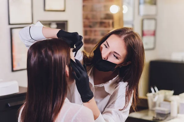 Beautician- maquiador aplica henna pintura em previamente arrancado, design, sobrancelhas aparadas em um salão de beleza na correção sessão. Cuidados profissionais para o rosto. — Fotografia de Stock