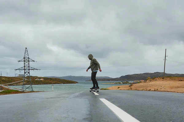 Młody człowiek jeżdżący longboard po pustej krętej górskiej drodze latem, widok z tyłu. — Zdjęcie stockowe