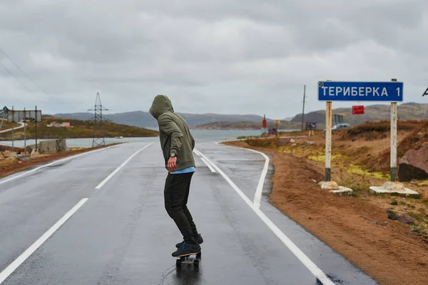 Młody człowiek jeżdżący longboard po pustej krętej górskiej drodze latem, widok z tyłu. — Zdjęcie stockowe