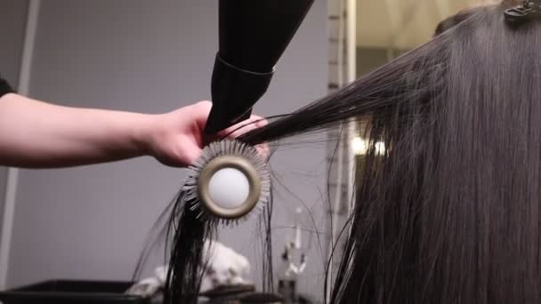 Close up of hairdressers hands drying long blond hair with blow dryer and round brush. — Stock Video