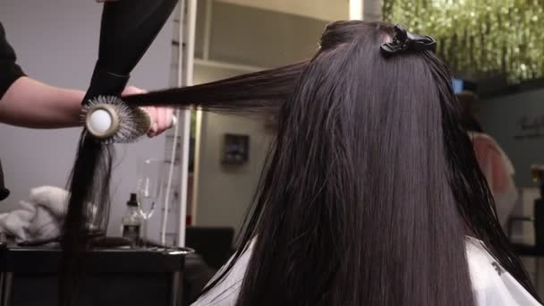 Крупним планом перукарські руки висушують довге світле волосся з сушаркою і круглою щіткою . — стокове відео