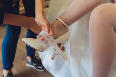 Sabah, gelinin çorapları ve beyaz gelinliği bacağına jartiyer takıyor, gelin jartiyer için elini tutuyor..