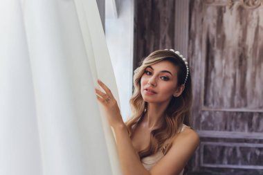 İç kısımda güzel sarışın bir gelinin portresi. Bornozlu genç gelin. Düğün fotoğrafçılığı. Gülümseyen ve tatlı kız duruyor.