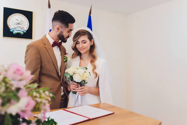 Recém-casados anexar assinaturas em um escritório de registro durante o registro do casamento . — Fotografia de Stock