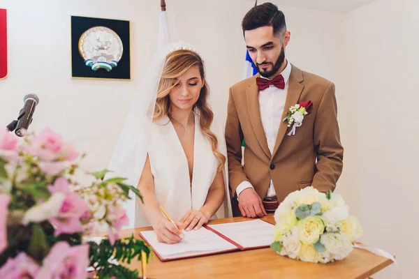 Nowożeńcy Dołącz podpisy w urzędzie stanu cywilnego w trakcie rejestracji ślubu. — Zdjęcie stockowe