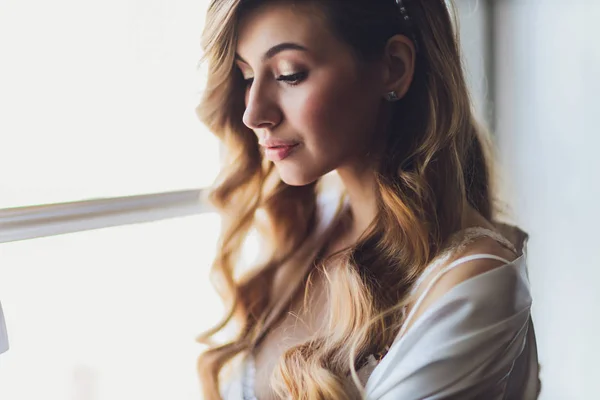 Portrait d'une belle mariée blonde à l'intérieur. Bonjour jeune mariée en peignoir. Photographie de mariage. Souriant et mignon fille se tient debout . — Photo