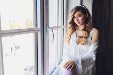 İç kısımda güzel sarışın bir gelinin portresi. Bornozlu genç gelin. Düğün fotoğrafçılığı. Gülümseyen ve tatlı kız duruyor.