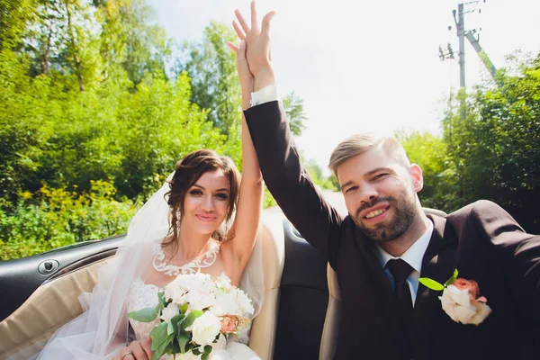 Closeup portrait young beautiful stylish couple bride in a white dress with a bouquet of flowers in her hair and and groom in car on the way. — Stock Photo, Image