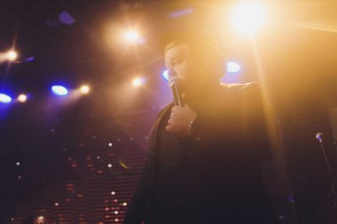 Şarkıcı ışıklarla aydınlatılmış sahnede şarkı söylüyor..