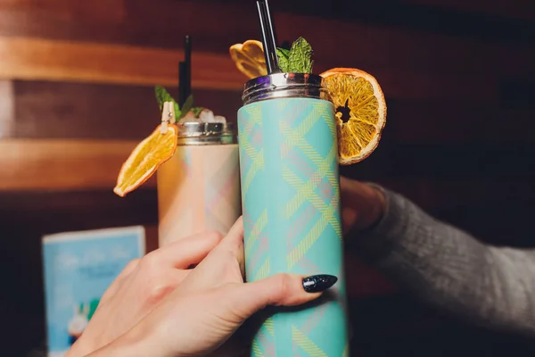 a refreshing drink stands on a table with a thermos of fruit and mint.