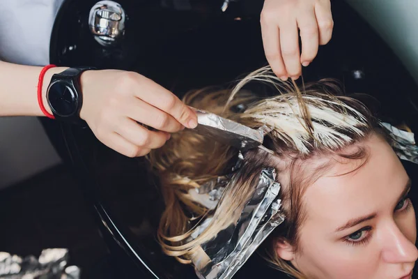 Closeup of hairdresser hands separating strands of hair of beautiful young woman with aluminium foil before change the hair color.