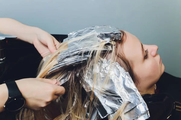 Primer plano de las manos de peluquero separando hebras de cabello de hermosa mujer joven con papel de aluminio antes de cambiar el color del cabello . — Foto de Stock