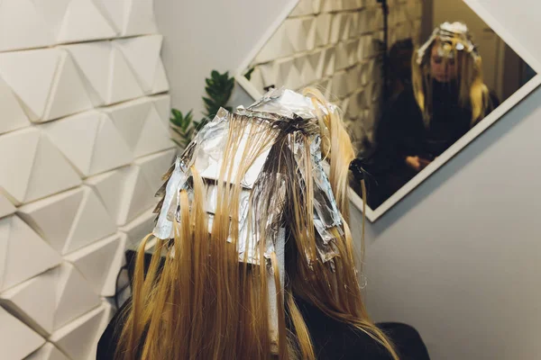 Primer plano de las manos de peluquero separando hebras de cabello de hermosa mujer joven con papel de aluminio antes de cambiar el color del cabello . — Foto de Stock