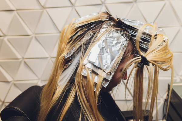 Крупный план парикмахерских рук, отделяющих пряди волос красивой молодой женщины с алюминиевой фольгой перед сменой цвета волос
.