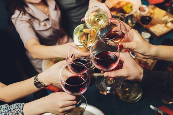 Close up shot of group of people clinking glasses with wine or champagne in front of bokeh background. older people hands.